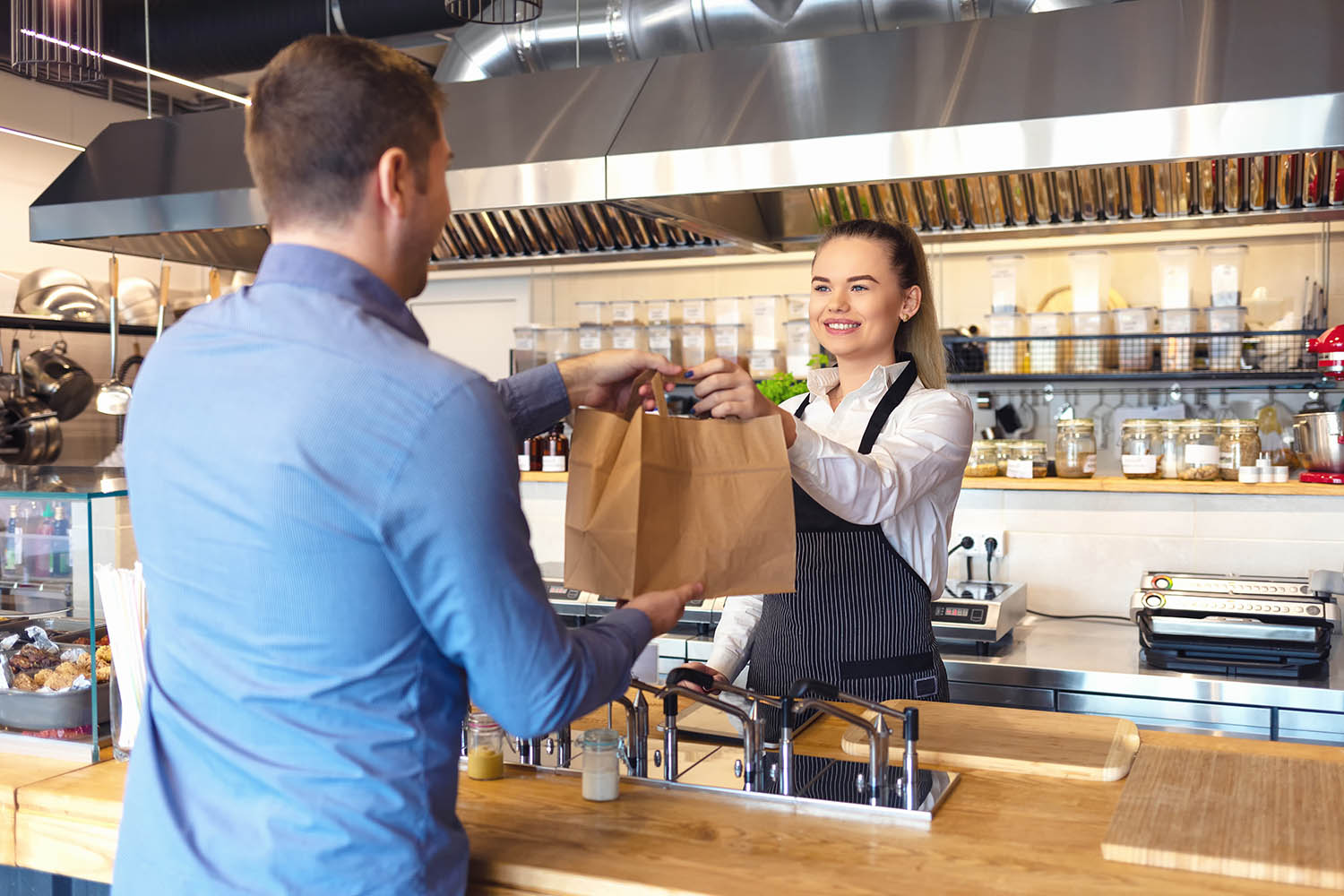 Happy waitress waring apron serving customer at counter in small